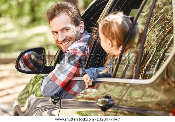 To\
travel is to live. Father and daughter looking out the car window\
and smiling happily to each other. Family road\
trip