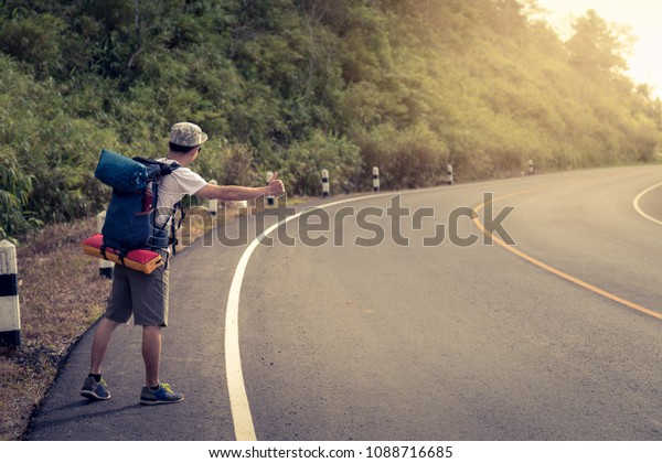Travel man hitchhiking. A hitchhiker by the\
road during vacation trip in mountains at sunset. The concept of\
traveling and\
hitchhiking.