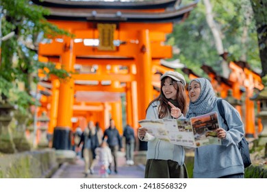 Travel, muslim, Two Asian female tourists of different religions friends visitor learning about history of fushimi inari shrine in travel book while walking through senbon torii path in Kyoto Japan. - Powered by Shutterstock