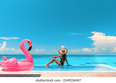 Travel on beach by pool on summer vacation in luxury resort. Woman relaxing in bikini by inflatable pink flamingo toy pool float on ocean turquoise background. Holiday travel destination concept. - Shutterstock ID 2149256947