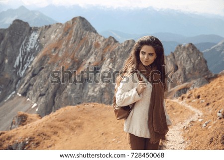 Travel Outfit of casual woman lifestyle. Brunette in knitting sweater enjoying nature above mountains view landscape. Outdoor look style. Girl wearing fashion white sweater and brown clothes.