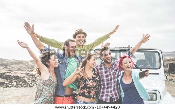 Travel people having fun taking selfie with
smartphone in desert at sunset  - Group of happy doing excursion
with convertible 4x4 car - Friendship and vacation concept - Main
focus on center guys