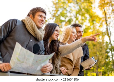 Travel, People, Tourism, Gesture And Friendship Concept - Group Of Smiling Friends With Map Standing On Bridge And Pointing Finger In City Park