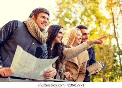 Travel, People, Tourism, Gesture And Friendship Concept - Group Of Smiling Friends With Map Standing On Bridge And Pointing Finger In City Park