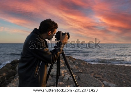 Travel photographer with digital camera making photo of the nature at sunset. Photographer and travel director on a seaside shooting with models looks into the viewfinder to take the best photo at sun