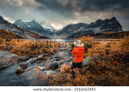 Travel photographer man taking a photo with camera at mount assiniboine in autumn wilderness by lake magog on moody day at Assiniboine provincial park, BC, Canada