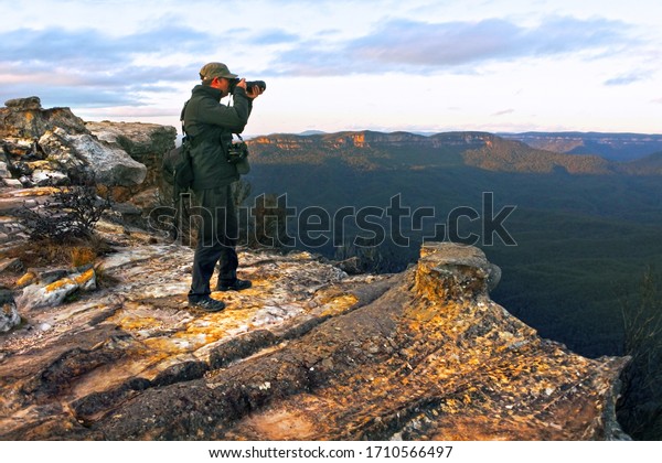 Travel photographer stands on a cliff and\
photographing the landscape from Lincoln Rock Lookout at sunrise in\
the Blue Mountains National Park in New South Wales, Australia.\
Real people. Copy space