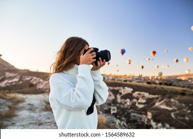 Travel photographer wearing white sweater taking a picture of balloons in Cappadocia. Travel photographer in Turkey