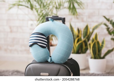 Travel pillow, sleep mask and suitcase on floor in room - Shutterstock ID 2054288768