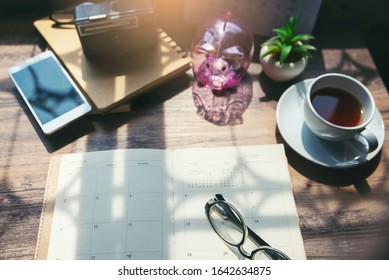 Travel Planning Concept.On Wooden Desk,Desktop Calendar,diary,laptop,piggy Bank,Cup Of Coffee,glasses And Old Film Camera Ready To Planner For Holiday Time In Summer,working Space From Home