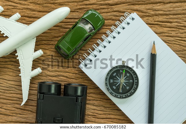 travel planning road trip concept with airplane,\
compass, binoculars, pencil, paper note and miniature car on wood\
table.