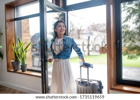 Travel plans. Dark-haired female opening glass door, pulling her suitcase, entering the house Zdjęcia stock © 