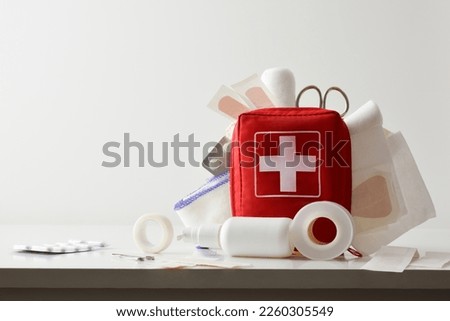 Travel portable first aid bag full of objects and tools for minor cures on white table. Front view. Horizontal composition