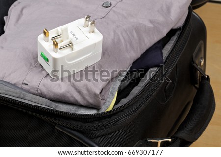 Travel power adapter with connectors for european, UK, and US power plugs on packed suitcase with clothings - travel preparation