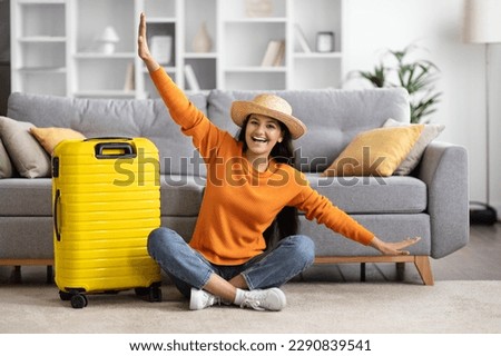 Travel preparation. Cheerful young eastern woman packing suitcase, getting ready for vacation at home, copy space. Female going on tourist trip, happy about abroad adventure, showing airplane