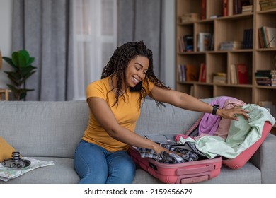 Travel Preparation Concept. Happy Black Woman Packing Suitcase And Getting Ready For Vacation, Sitting On Sofa At Home. African American Lady Going On Tourist Trip