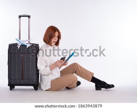 Travel preparation. The girl is booking a hotel. A girl with a smartphone is sitting next to a suitcase. Ready to travel. Last-minute deals. Last-minute tours.