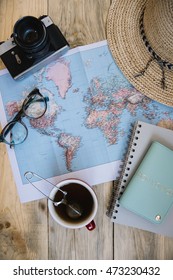 Travel Preparations Essentials. World Map, Cup Of Tea, Vintage Film Camera, Hat, Passport, Notebook And Stylish Glasses On The Old Rustic Wooden Table Background, Flat Lay