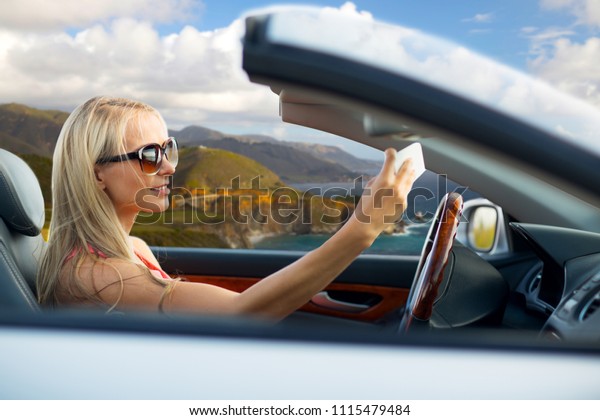travel, road trip and people concept - happy\
young woman in convertible car taking selfie by smartphone over big\
sur coast of california\
background