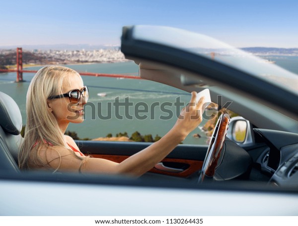 travel, road trip and people\
concept - happy young woman in convertible car taking selfie by\
smartphone over golden gate bridge in san francisco bay\
background