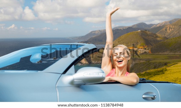 travel, road trip and people concept - happy\
young woman in convertible car waving hand over bixby creek bridge\
on big sur coast of california\
background