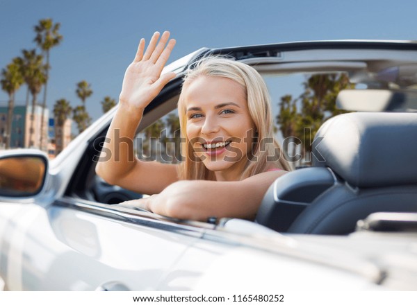 travel, road trip and people concept - happy
young woman in convertible car waving hand over venice beach
background in
california