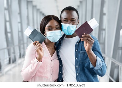 Travel Safe During Coronavirus Pandemic. Black Couple In Protective Medical Masks Posing With Passports And Tickets At Airport, Closeup