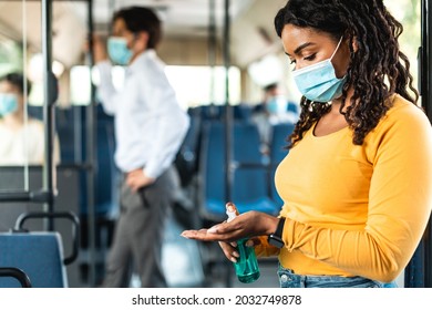 Travel Safely On Public Transport. Young Black Woman In Protective Face Mask Using Wash Hand Sanitizer Gel Dispenser. Female Passenger Disinfects Hands In Bus. Covid Pandemic, Hygiene, New Normal