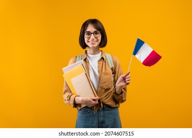 Travel and student exchange. Happy young woman in glasses with notebooks, backpack, holding small flag of France, posing on orange background, studio shot - Powered by Shutterstock