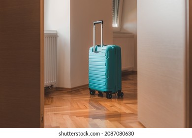 Travel suitcase behind the open door of hotel apartment room, selective focus