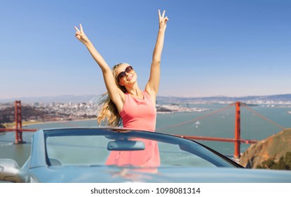 Travel, Summer Holidays, Road Trip And People Concept - Happy Young Woman Wearing Sunglasses In Convertible Car Showing Peace Hand Sign Over Golden Gate Bridge In San Francisco Bay Background