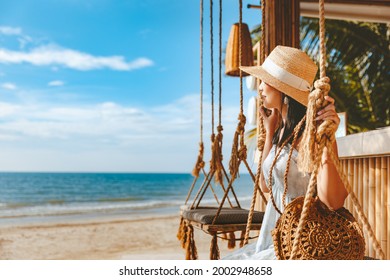 Travel summer vacation concept, Happy traveler asian woman with hat and dress relax on swing in beach cafe, Koh Chang, Thailand