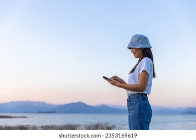 Travel summer vacation concept, Happy young asian solo traveler woman using mobile phone in lake at sunset in Phetchaburi, Thailand - Powered by Shutterstock