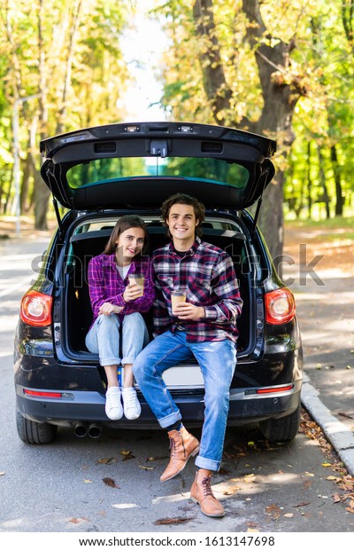 travel, summer vacation, road
trip, leisure and people concept - happy couple drinking coffee
from disposable cups sitting on trunk of hatchback car
outdoors