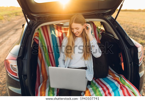 Travel and\
technology. Happy young woman working on laptop celebrating victory\
while sitting in trunk of\
car
