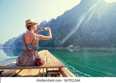Travel and technology. Pretty young woman taking photo on smartphone sailing National Park lake on traditional bamboo raft. - Powered by Shutterstock