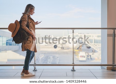 Travel and technology. Pretty young woman using smartphone waiting for boarding in airport terminal.