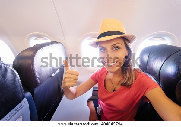Travel and technology. Young woman in\
plane taking selfie while sitting in airplane\
seat.