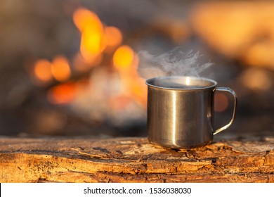 Travel Titanium Cup On Wood On Fire Background. Lunch During Journey To The Wild. Camping Lifestyle, Copy Space