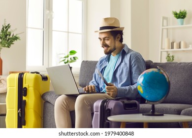 Travel And Tour Agency Online Service Concept. Happy Smiling Man In Summer Hat Holding Ticket And Passport Using Laptop Digital Interface For Hotel Booking Or Reservation From Home On Vacation