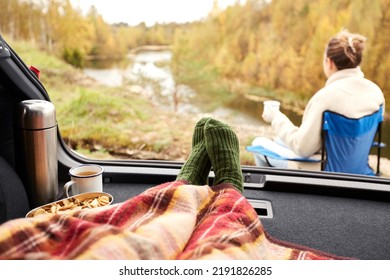 travel, tourism and camping concept - view to river from car trunk with feet in warm socks under blanket, two cups of tea, thermos and cookies - Powered by Shutterstock