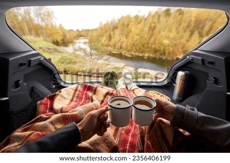 travel, tourism and camping concept - view to river from car trunk with couple under blanket toasting tea cups