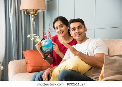 Travel And Tourism Concept - Asian Indian Young Couple Planning Vacation Trip With 3d Globe Model While Sitting On Sofa Or Couch