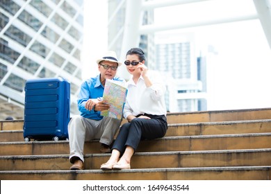 Travel And Tourism Concept. Senior Asian Couple Traveling Siting Stairs And Together Looking For Destination With City Map