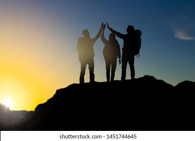travel, tourism and hike concept - group of travelers with backpacks making high five on mountain top over sunrise background