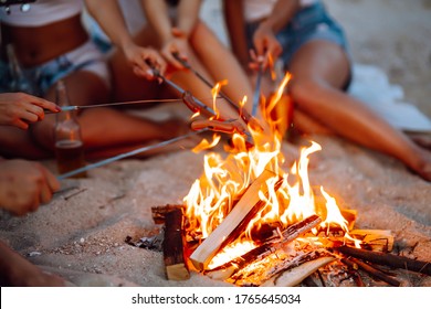 Travel, tourism, hike, picnic and people concept - group of happy friends frying sausages on campfire at the beach. A company of young people came together for a barbecue. - Powered by Shutterstock