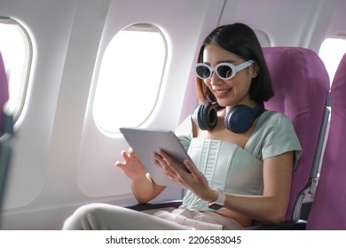 Travel Tourism With Modern Technology And Air Flights Concept, Woman Sitting In Plane With Modern Digital Gadget And Searching Favourite Music Playlist In Application For Listening
