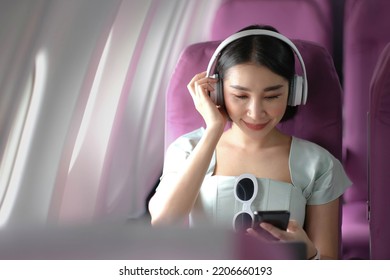 Travel Tourism With Modern Technology And Air Flights Concept, Woman Sitting In Plane With Modern Smartphone And Searching Favourite Music Playlist In Application For Listening
