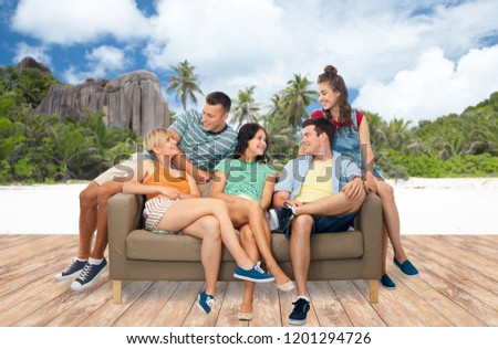 travel, tourism and people concept - group of happy smiling friends sitting on sofa over tropical beach on seychelles island background