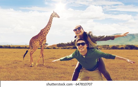 travel, tourism and people concept - happy couple with backpacks having fun over giraffe in african savannah background